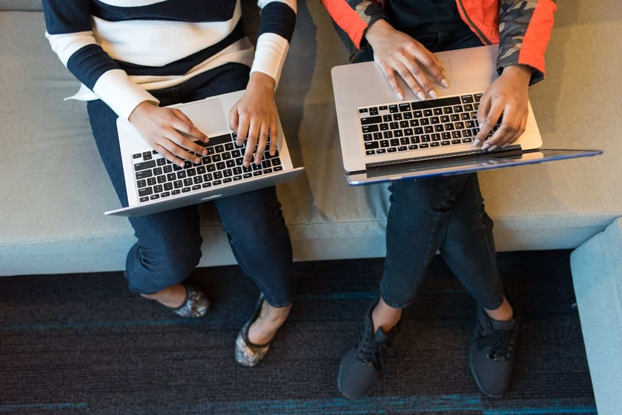 Two individuals collaborating on laptops while seated on a couch.
