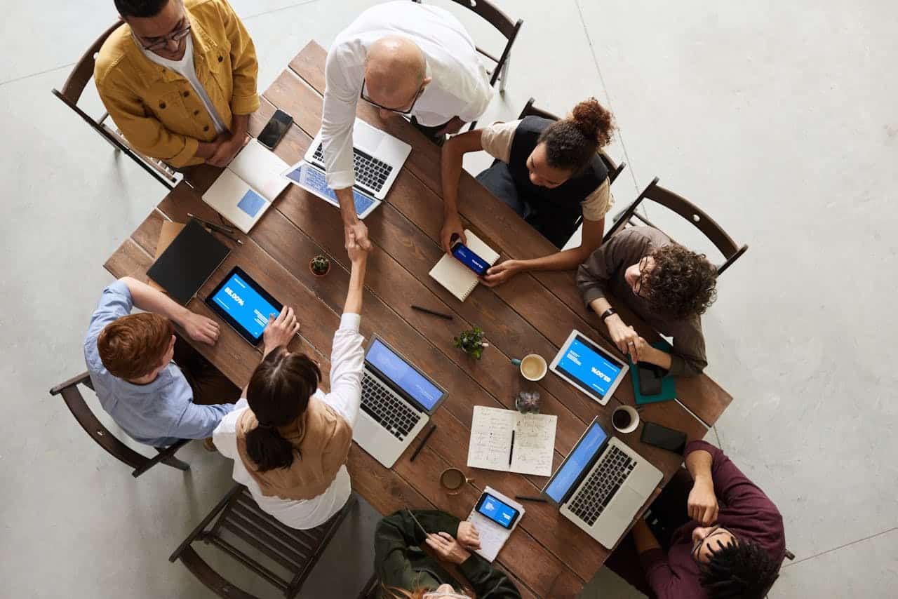 Aerial view of a diverse team collaborating during a meeting with laptops and tablets on a wooden table.