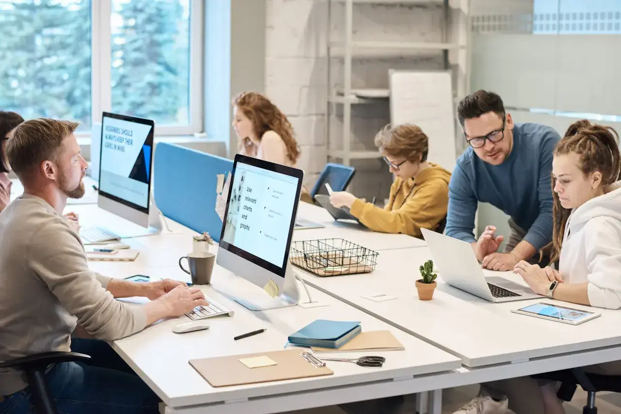 Team members collaborating in a modern office setting with computers and laptops.